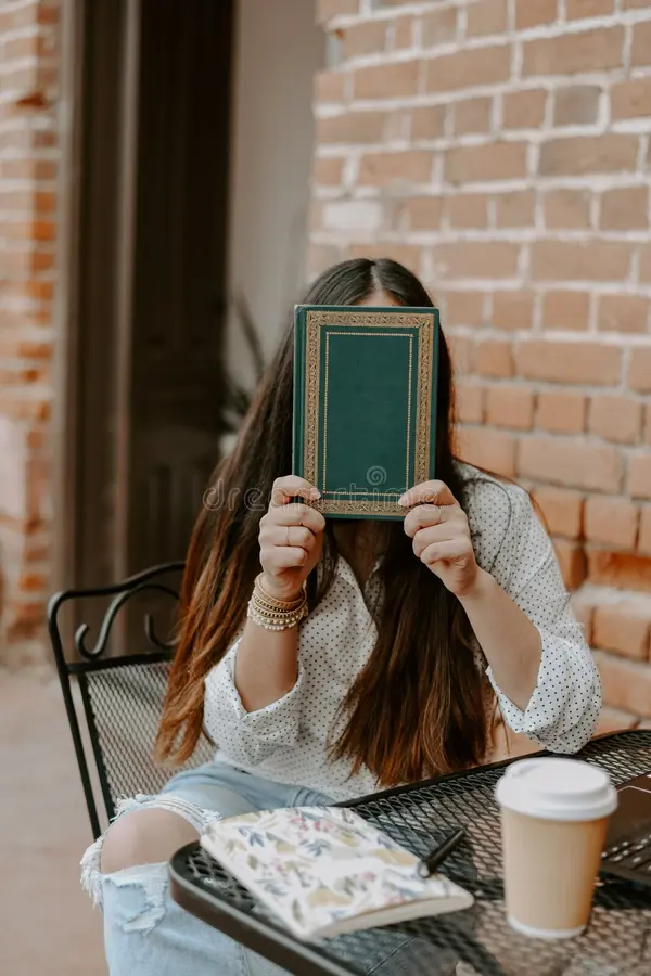 A female sitting in a cafe, her face hidden at the back of an e-book